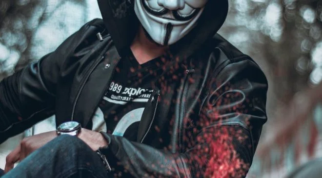 person wearing guys fawkes mask watching flame