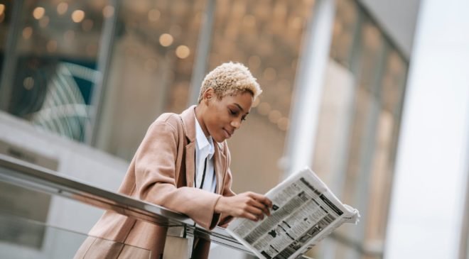 content black woman reading newspaper outside modern business center